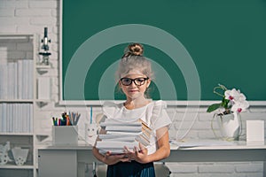 Cute child at school. Kid is learning in class on background of blackboard. Nerd school girl in glasses with books on