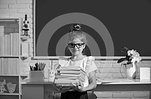 Cute child at school. Kid is learning in class on background of blackboard. Nerd school girl in glasses with books on