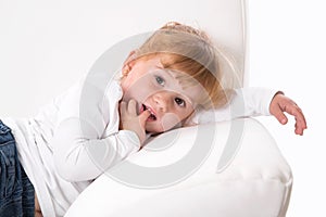 Cute child - shy girl lying on white sofa sucking thumb or finger