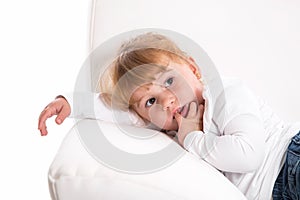 Cute child - shy girl lying on white sofa sucking thumb or finger