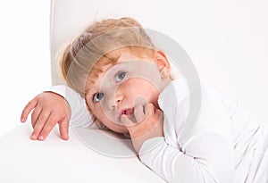 Cute child - shy girl lying on white sofa sucking thumb or finger