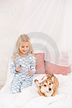Cute child sitting on bed with corgi dog and photo