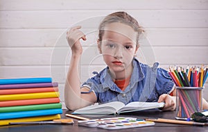 Cute child is sitting at a desk indoors. Kid is drawing in class on background of blackboard.
