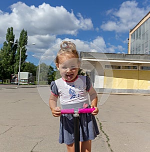 Cute child skilfully skates on a pink two-wheeled scooter on a s