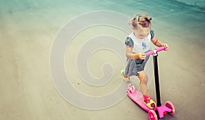 Cute child skilfully skates on a pink two-wheeled scooter on a s