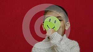 Cute child smiling and expressing his happiness with green happy emoji. Isolated on red background,