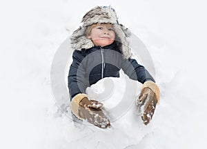 Cute child standing in winter hat with red nose. Joyful kid Having Fun and making snowman in Winter Park. Winter clothes