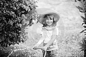 Cute child in straw hat is laughing with water spraying hose.