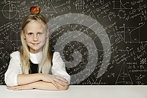 Cute child student girl with red apple on head. Blackboard background with science formulas. Learning science concept