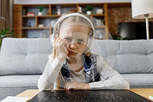 Cute child studying remotely at home using laptop. Tired primary schoolgirl falling asleep during an online lesson with