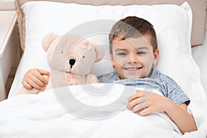 Cute child with teddy bear resting in bed