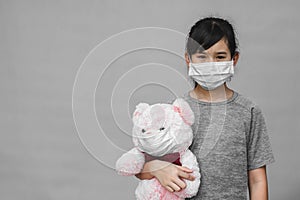 Cute child with teddy bear in wearing surgical mask isolated on gray background.