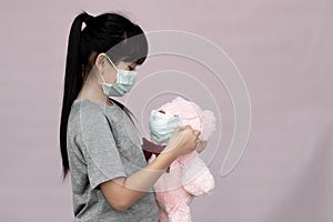 Cute child with teddy bear in wearing surgical mask isolated on gray background.