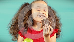 Cute Child on Turquoise Background of Holding a Green Apple and Chocolate and Choice Healthy Eating between Fruit and