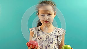 Cute Child on Turquoise Background of Holding a Green Apple and Red Aplle and Choice Healthy Eating.Little Kid Makes a