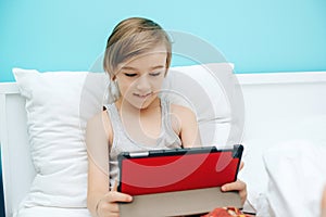 Cute child using digital gadget in bed before going to sleep. Boy watches video and plays games on tablet