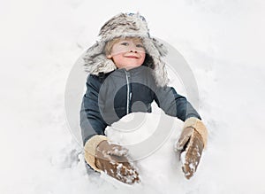 Cute child in winter hat having fun with snowball in winter park. Winter clothes for kids.