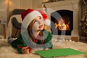 Cute child writing letter to Santa Claus while lying on floor at home. Christmas celebration