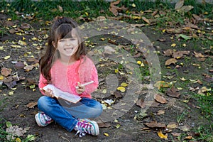 Cute child writing in notebook using pen and smiling. Four years old kid sitting on grass
