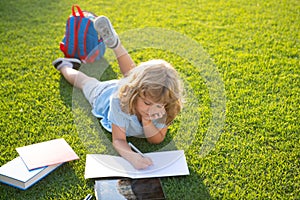 Cute childr boy writing notes in copybook with books outdoors. Kids learning and education concept. Preparation for