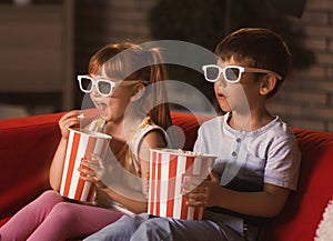 Cute children in 3d glasses watching movie on sofa in evening