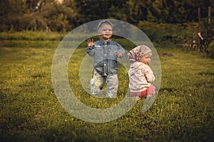 Cute children boy and girl playing together on grass at sunset in rural field in countryside symbolizing carefree and ha