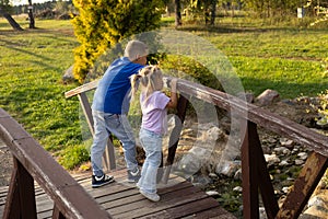 Cute children boy and girl are standing on a wooden bridge over a small river. children admire the flow of water while