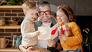 Cute children congratulating happy daddy with Fathers day and giving him handmade greeting postcard