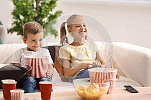 Cute children eating popcorn while watching TV at home