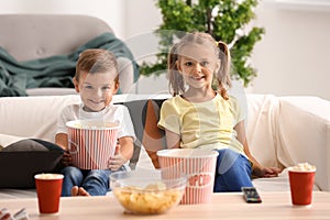 Cute children eating popcorn while watching TV at home