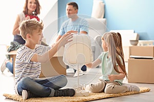 Cute children with lamp sitting on rug indoors. Moving into new house