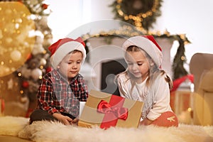 Cute children opening gift box in room decorated for Christmas