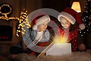 Cute children opening gift box in room decorated for Christmas