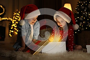 Cute children opening gift box in room decorated for Christmas