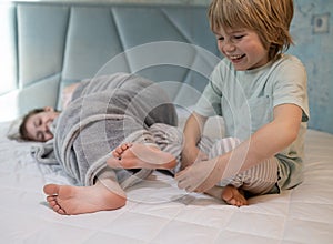 cute children in pajamas play around on the bed at home. brother tickles sister's bare feet