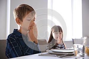 Cute children praying before meal at home