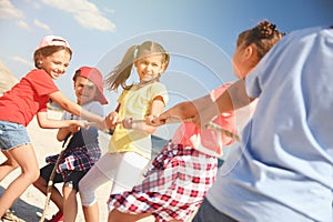 Cute children pulling rope during tug of war game on beach. Summer camp