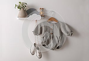 Cute children`s baby onesie and shoes hanging on white wall