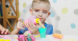 Cute children sitting at the table and plays with playdough