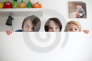 Cute children, three boy brothers, hiding in bed, only eyes peeping out above the wooden board