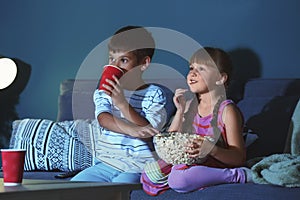 Cute children watching TV on sofa in evening