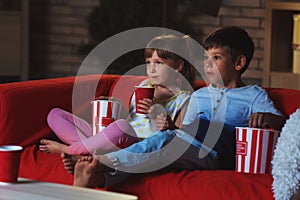 Cute children watching TV on sofa in evening