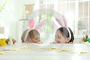 Cute children wearing bunny ears headbands at table with Easter eggs