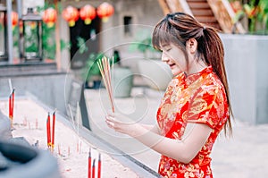 Cute chinese girl dressing traditional red Cheongsam suit burning incense sticks and pay respect and praying to Chinese God