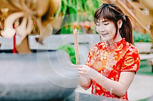 Cute chinese girl dressing traditional red Cheongsam suit burning incense sticks and pay respect and praying to Chinese God