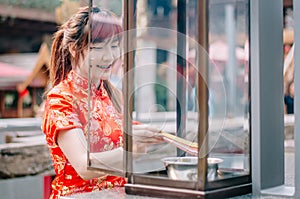 Cute chinese girl dressing traditional red Cheongsam suit burning incense sticks and pay respect and praying to Chinese God