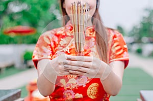 Cute chinese girl dressing traditional red Cheongsam suit burning incense sticks and pay respect and praying to Chinese God