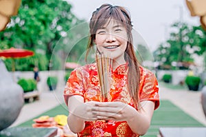 Cute chinese girl dressing traditional red Cheongsam suit burning incense sticks and pay respect and praying to Chinese God