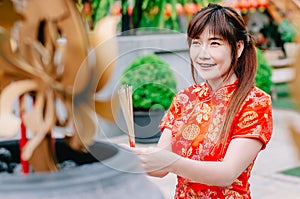 Cute chinese girl dressing traditional red Cheongsam suit burning incense sticks and pay respect and praying to Chinese God