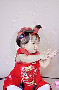 Cute Chinese little baby in red cheongsam play soap bubbles